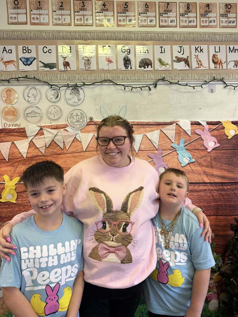 Two young boys have easter shirts on that say "Chillin' with my peeps" and their teacher has a shirt on that has a bunny rabbit on it. 