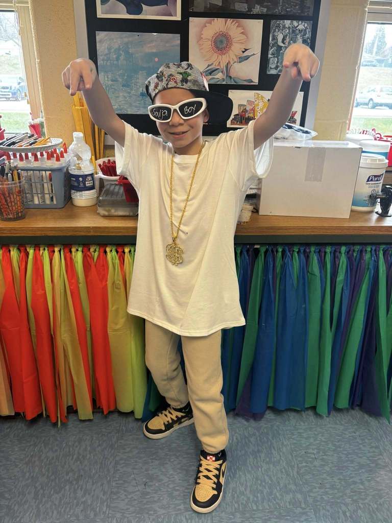 A student wearing glasses, an over sized white shirt, a hat that is sideways, and a chain for 2000's wear.