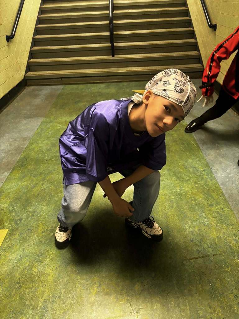 A young boy wearing a bandana and a purple over sized shirt for 2000's wear. 