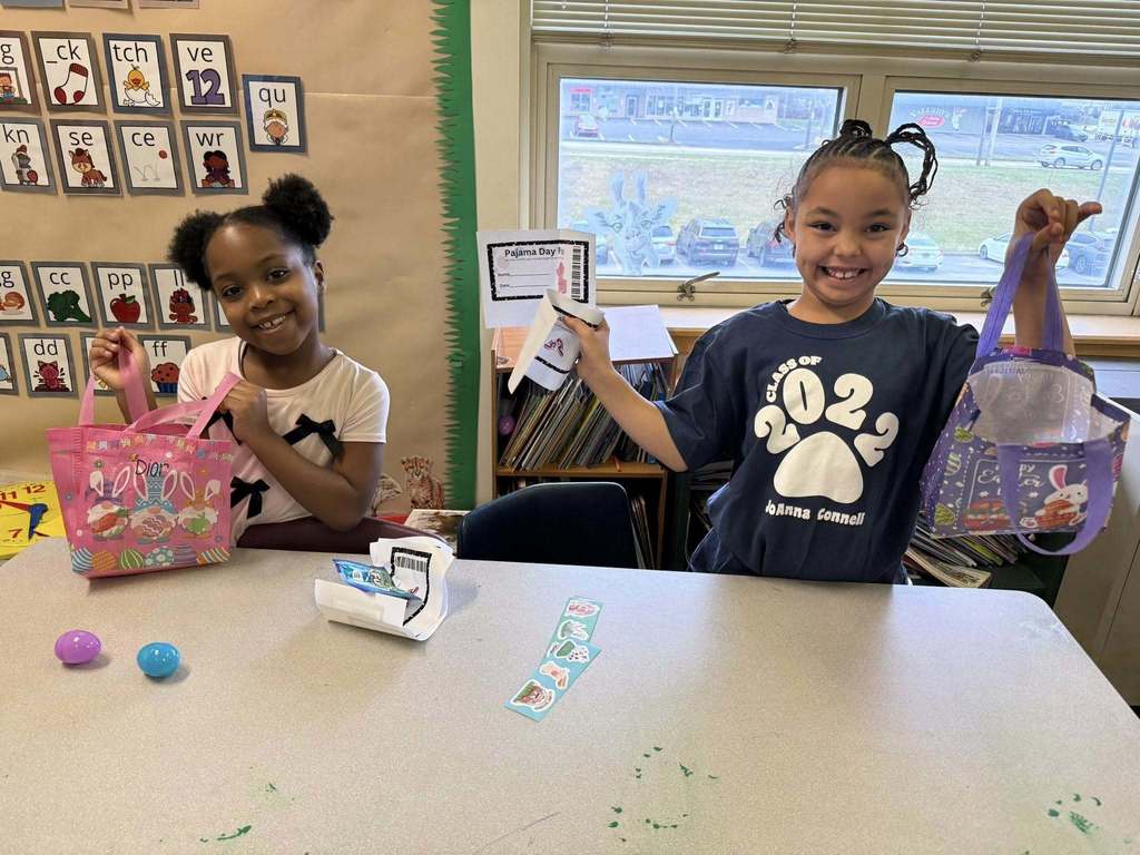 Two young student is holding their Easter bag with goodies in it on their desk and smiling for a photo. 