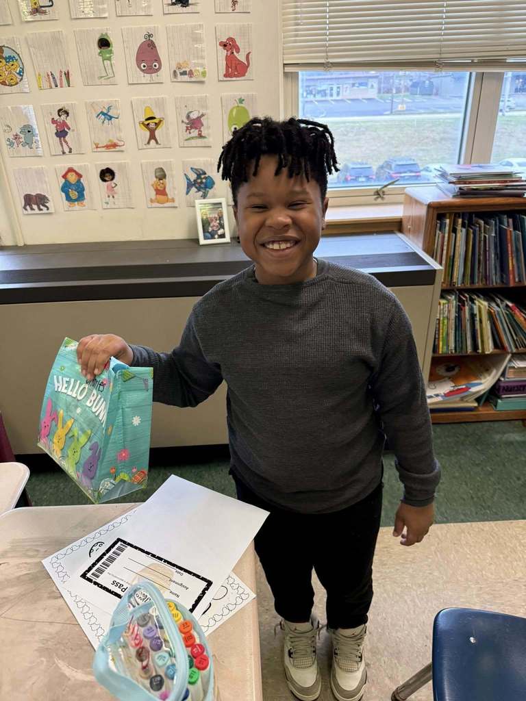 A young student is holding their Easter bag with goodies in it and smiling for a photo. 