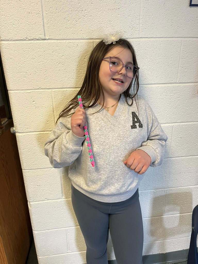 A young girl who is wearing a gray shirt with the letter "A" on it,  is holding a blue and pink fidget toy she won during bingo.