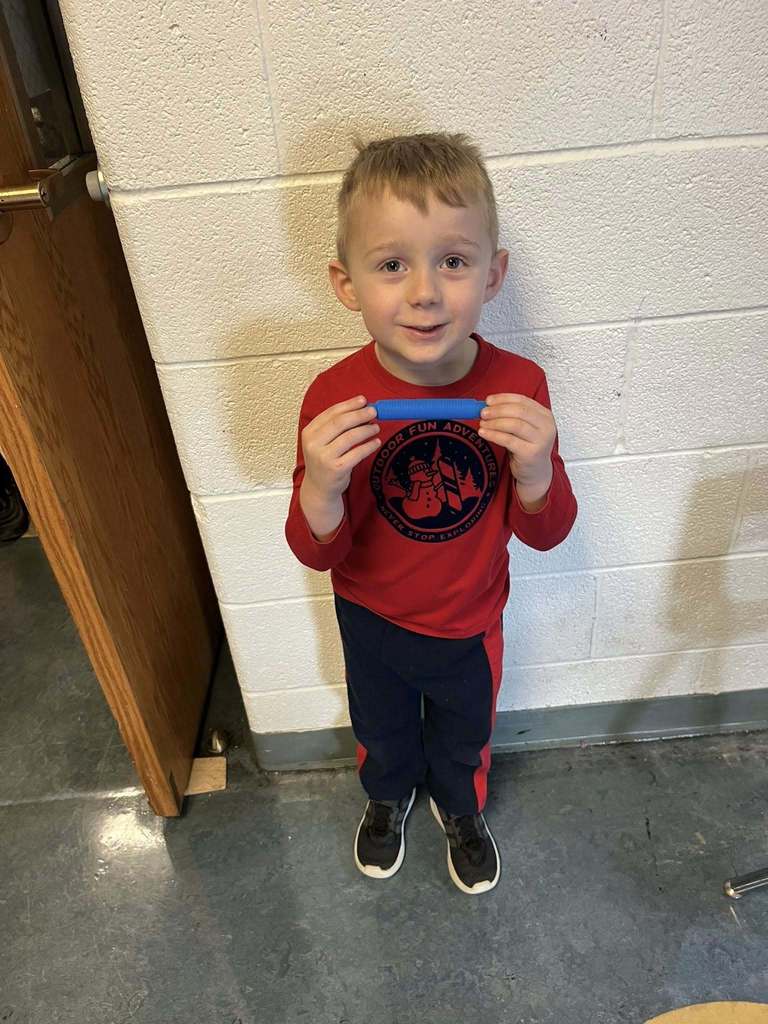 A young boy who is wearing a red shirt is holding a blue fidget toy he won during bingo.