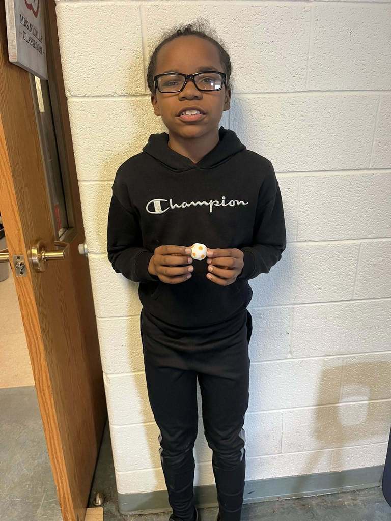 A young boy wearing a black champion hoodie is holding a white and orange fidget ball. 