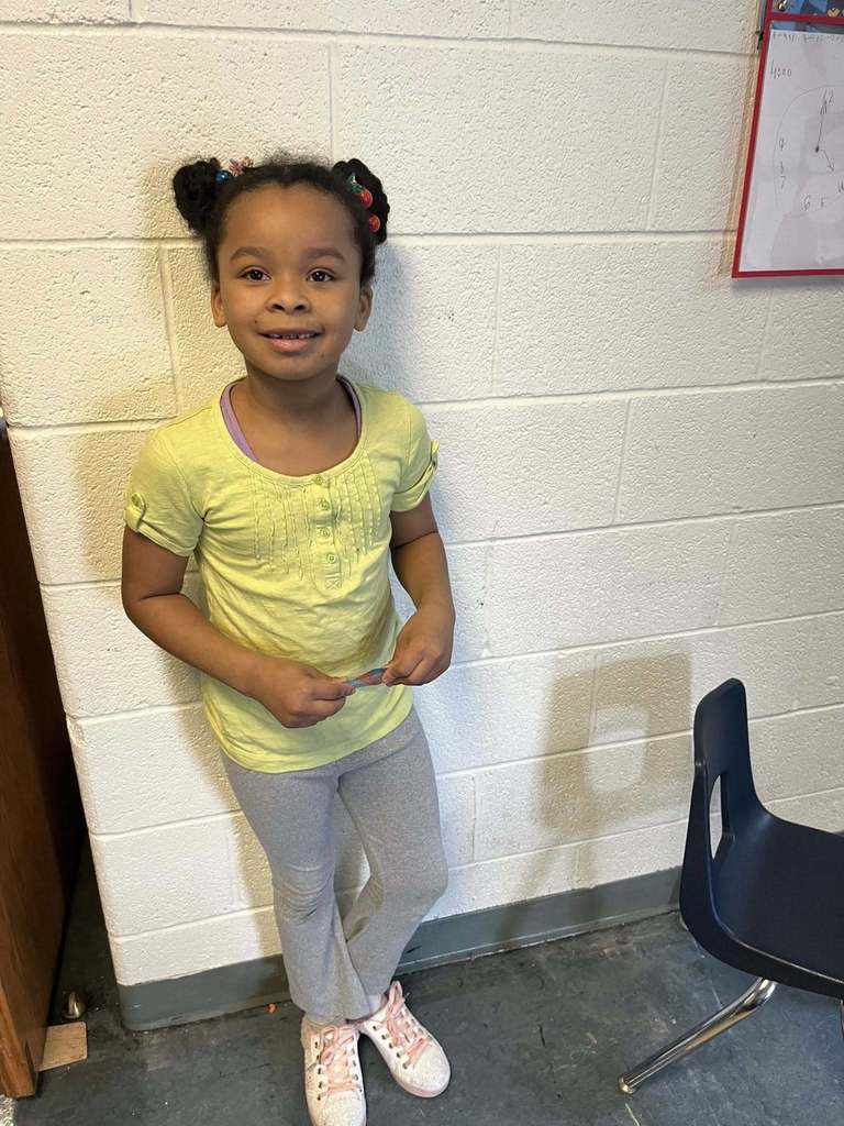 A young girl who is wearing a yellow shirt is posing for a photo.
