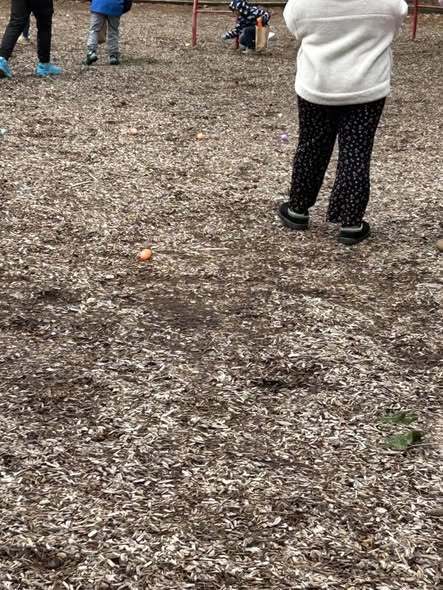 An orange egg on the floor behind a person who is wearing a white jacket. 