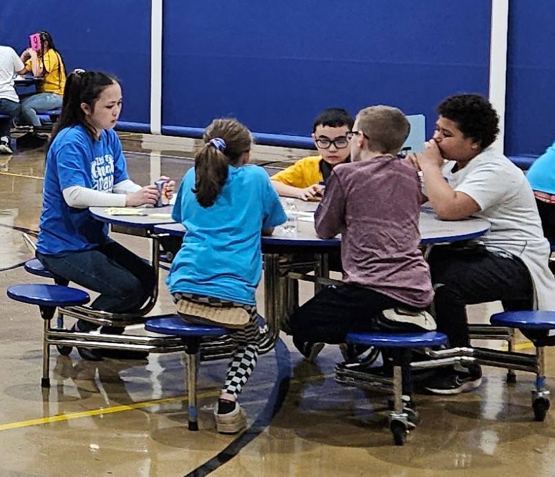 Students and adult at a circular table. 