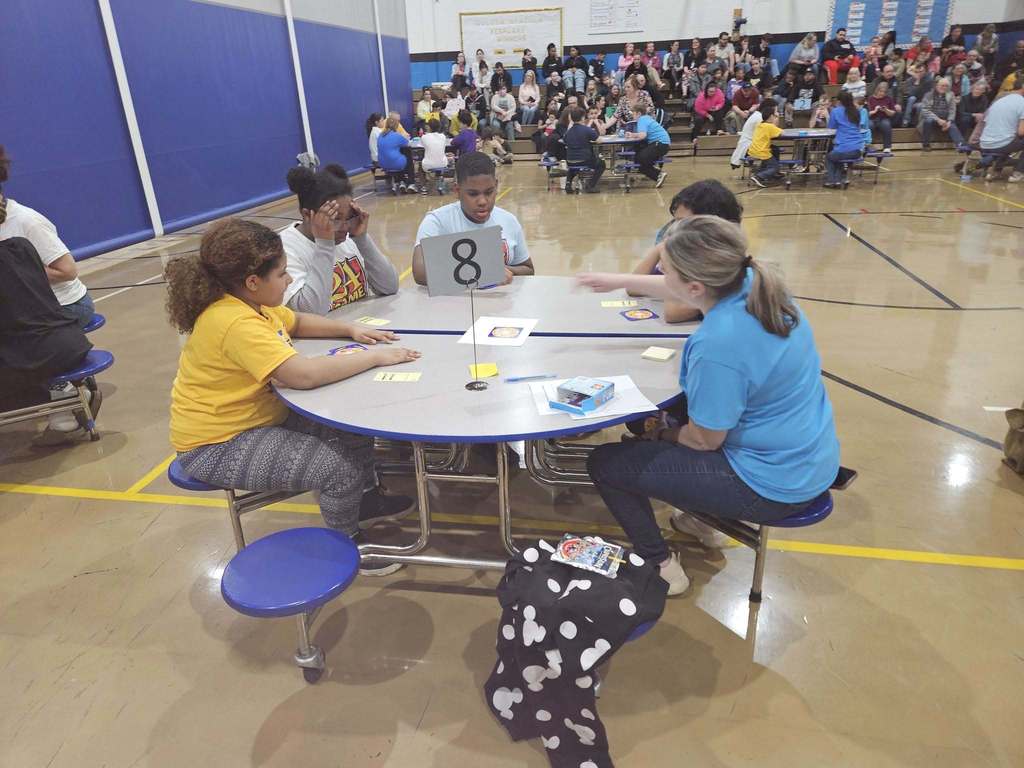 Students and adult at a circular table doing an activity. 