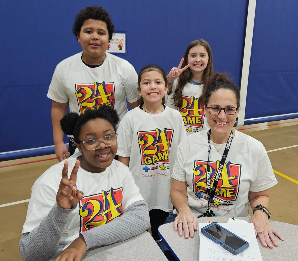 Students and adult wearing matching white shirts that say "24 Game" on them and they are posing for a photo. 