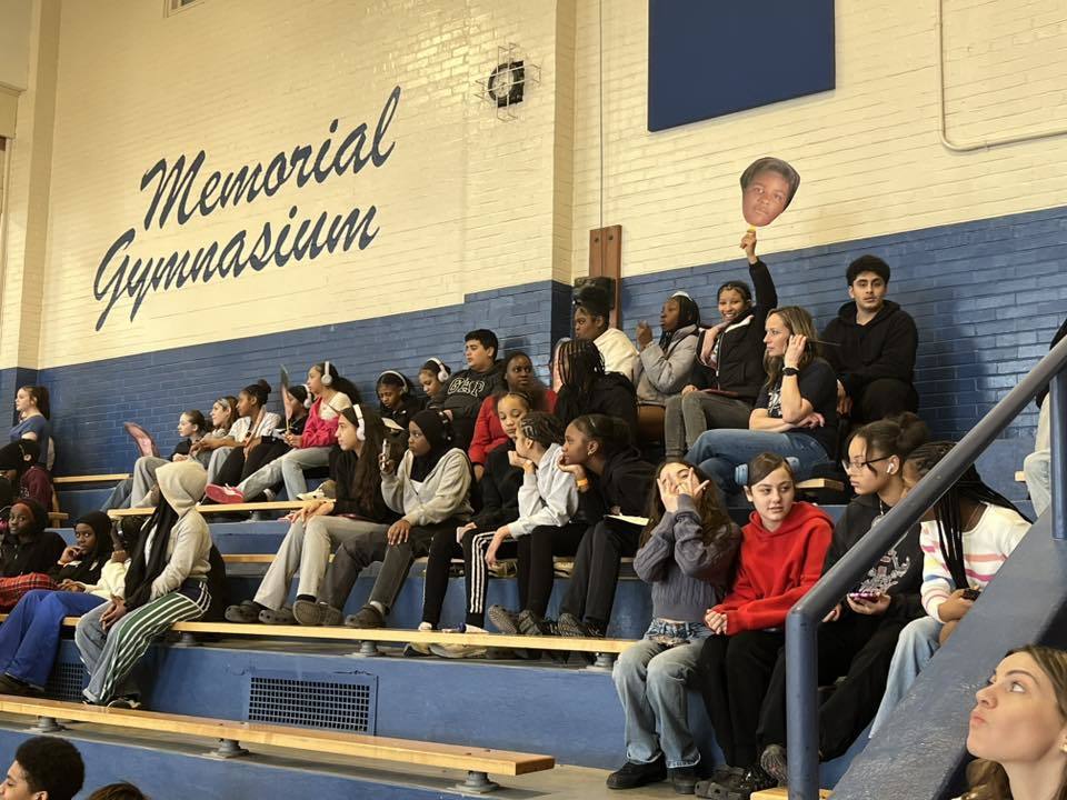 People sitting in the bleachers and cheering on the people playing the basketball game. 