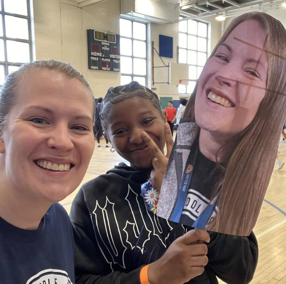 A women posing next to a student who has a cut out of her face. 