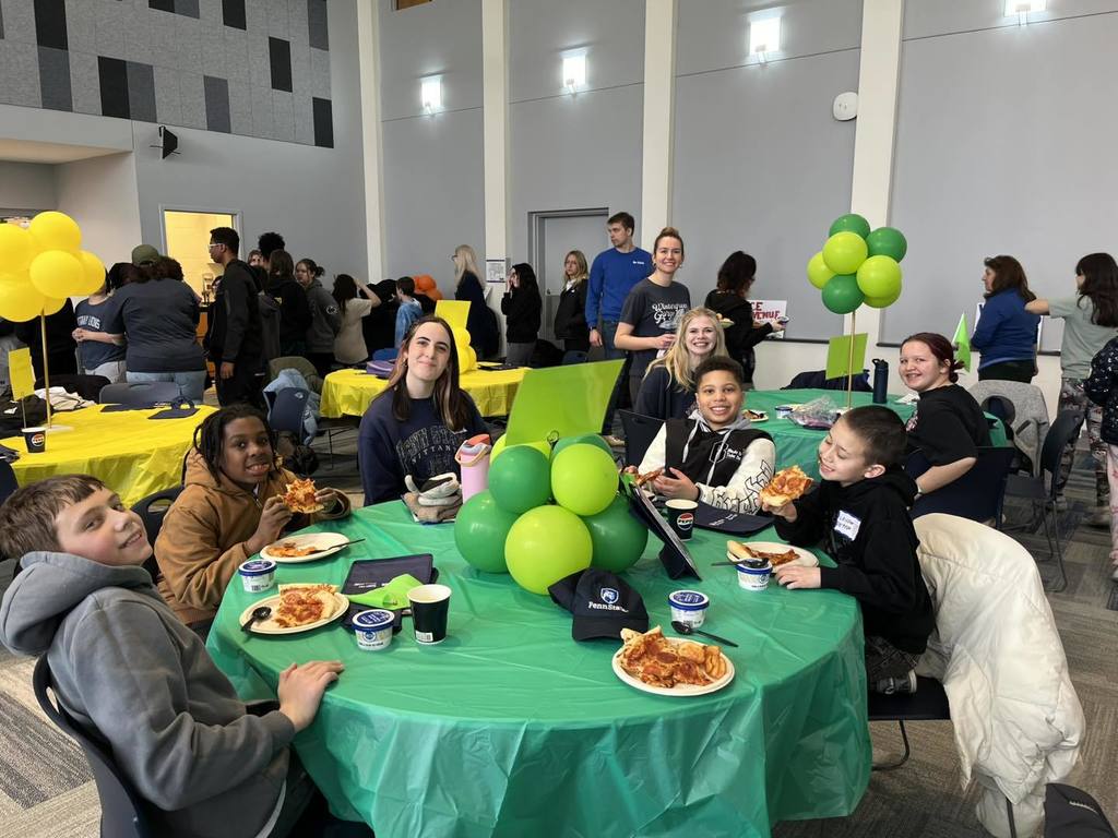 Students and staff eating at pizza and posing for a photo. 