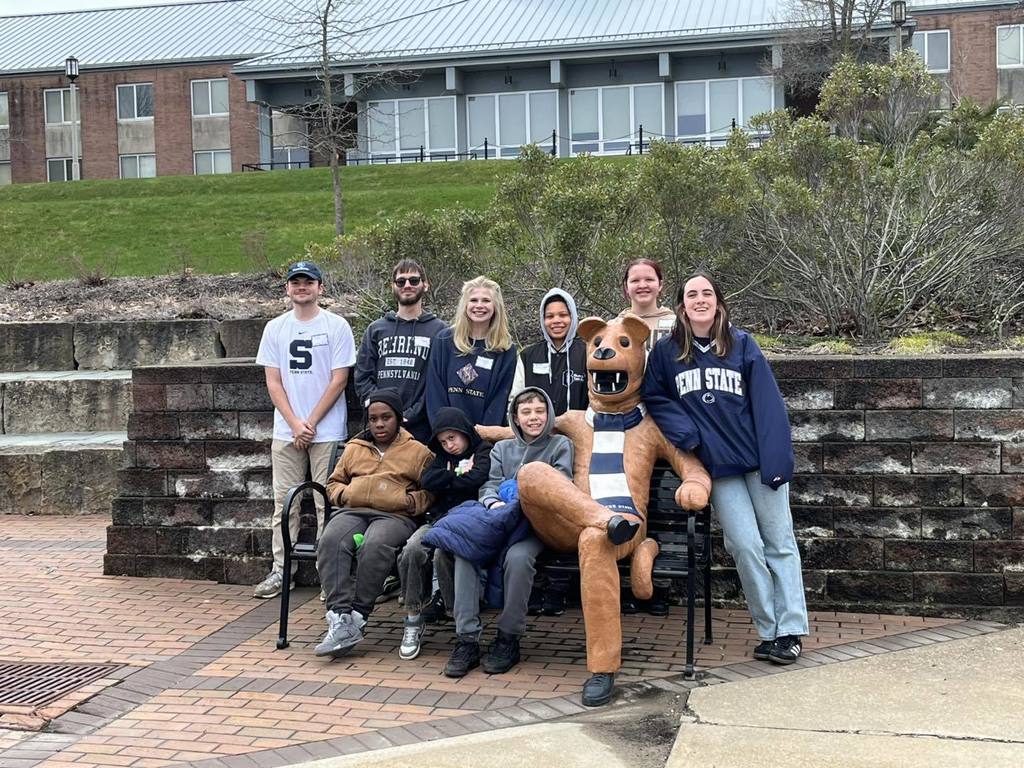 A group photo of students from Wilson Middle School and Penn State Behrend Students posing with the Penn State Lion on the bench. 