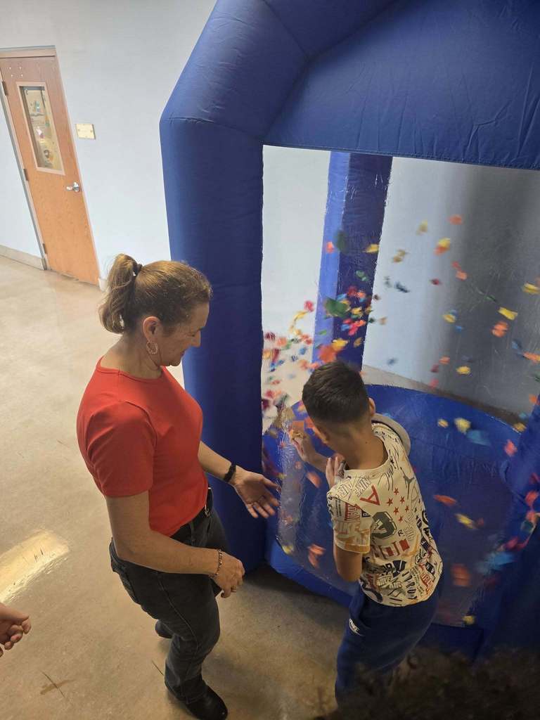 A student has his hand in a blow up tunnel and he is trying to catch as many points as they can which is written on the paper that is flying around in the blow up tunnel. 