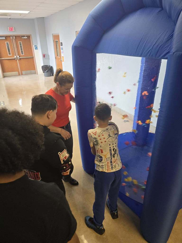 A student has his hand in a blow up tunnel and he is trying to catch as many points as they can which is written on the paper that is flying around in the blow up tunnel. 
