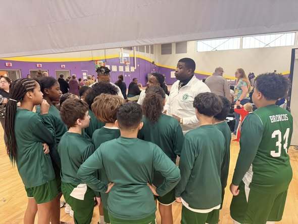A team in green is listening to a man talk to them before a game. 