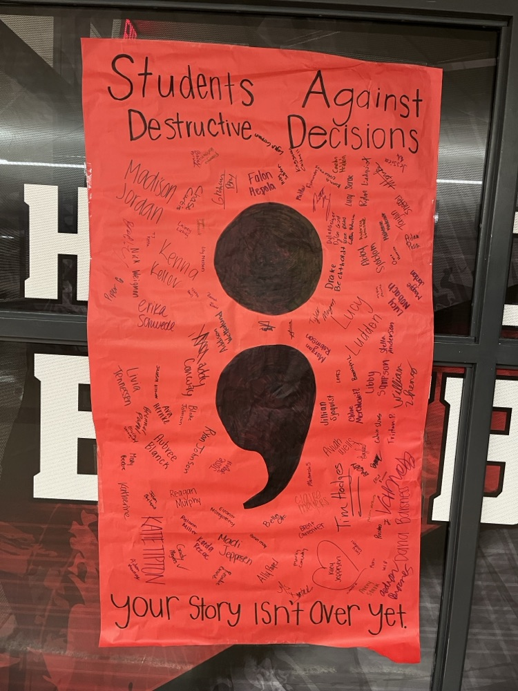 red posterboard with large semicolon in the middle, and signatures surrounding it 