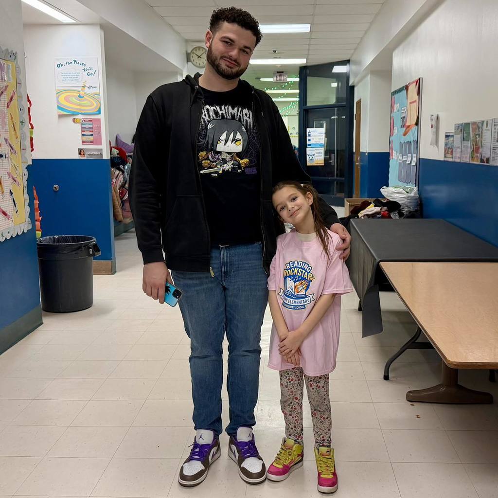 A young girl in a pink shirt is standing next to a man and smiling. 