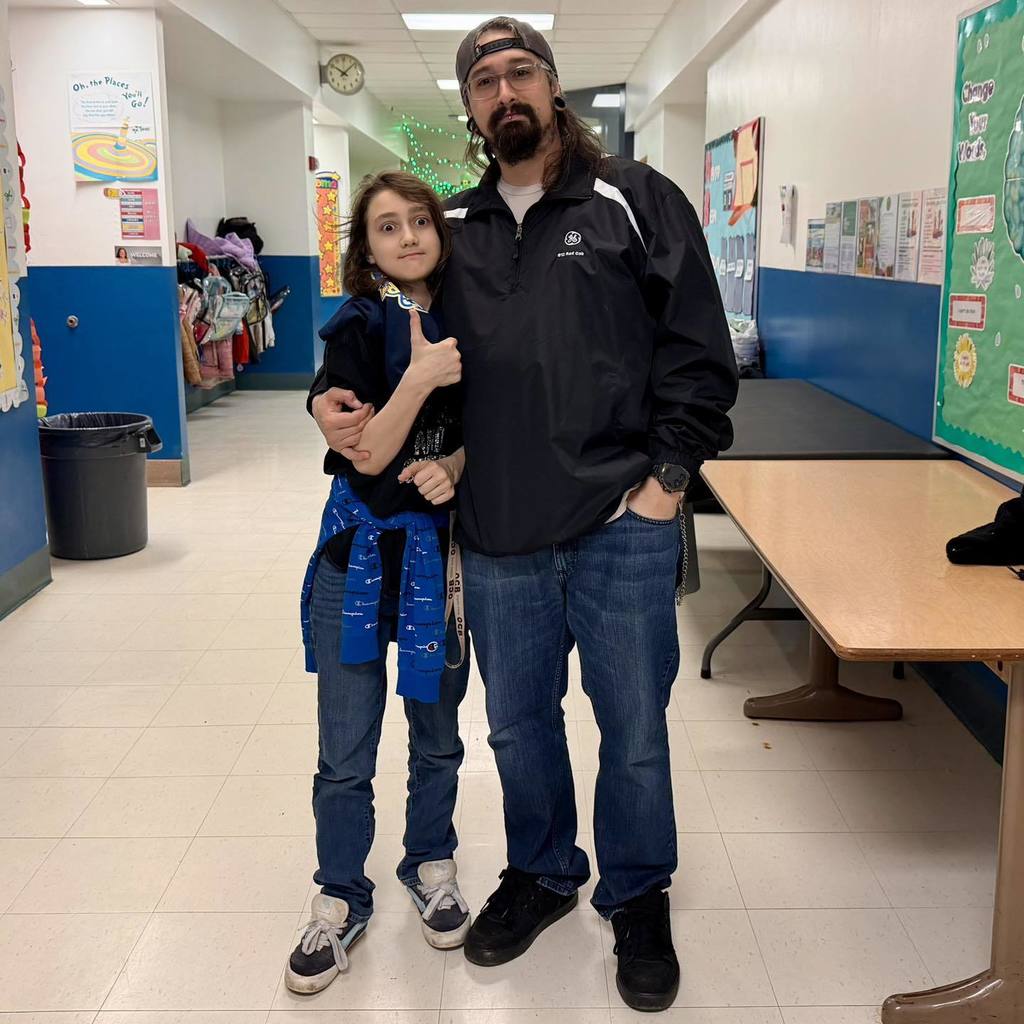 A student in a black shirt is standing next to a man and smiling. 