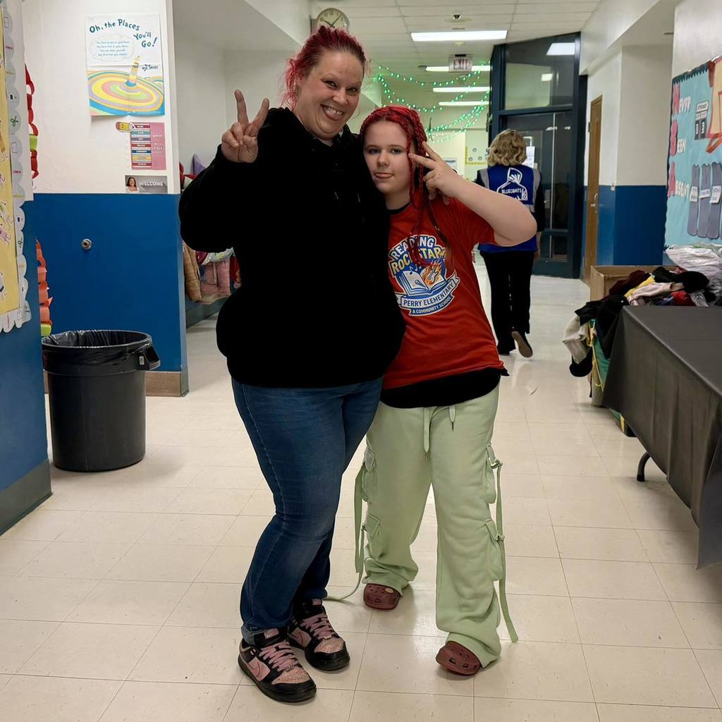 A student in a red shirt is standing next to a women and they are both holding up peace signs. 
