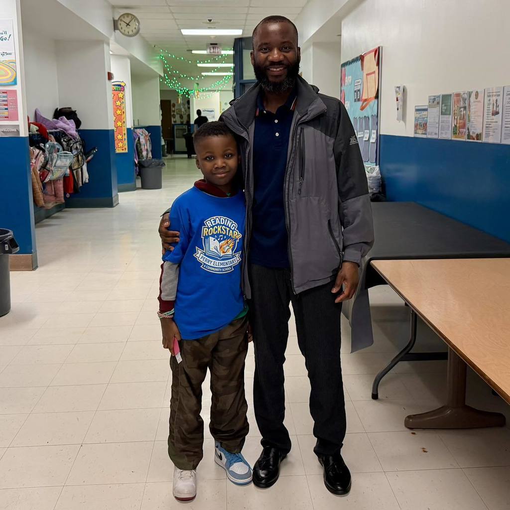 A student in a blue shirt is standing next to a man and smiling. 