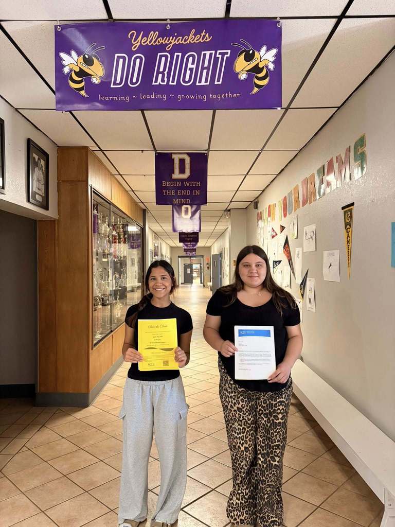Two women stand in a school hallway holding certificates. A banner above reads "Yellowjackets Do Right." Various decorations adorn the walls.