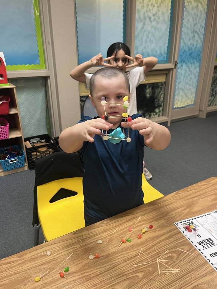 A student holding an easter peep inside a house he made of toothpicks and jelly beans.