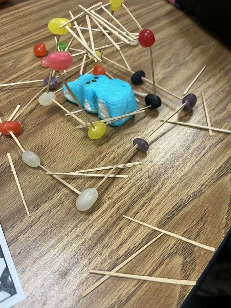 An easter peep inside a house made of toothpicks and jelly beans.