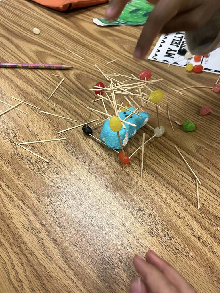 An easter peep inside a house made of toothpicks and jelly beans.