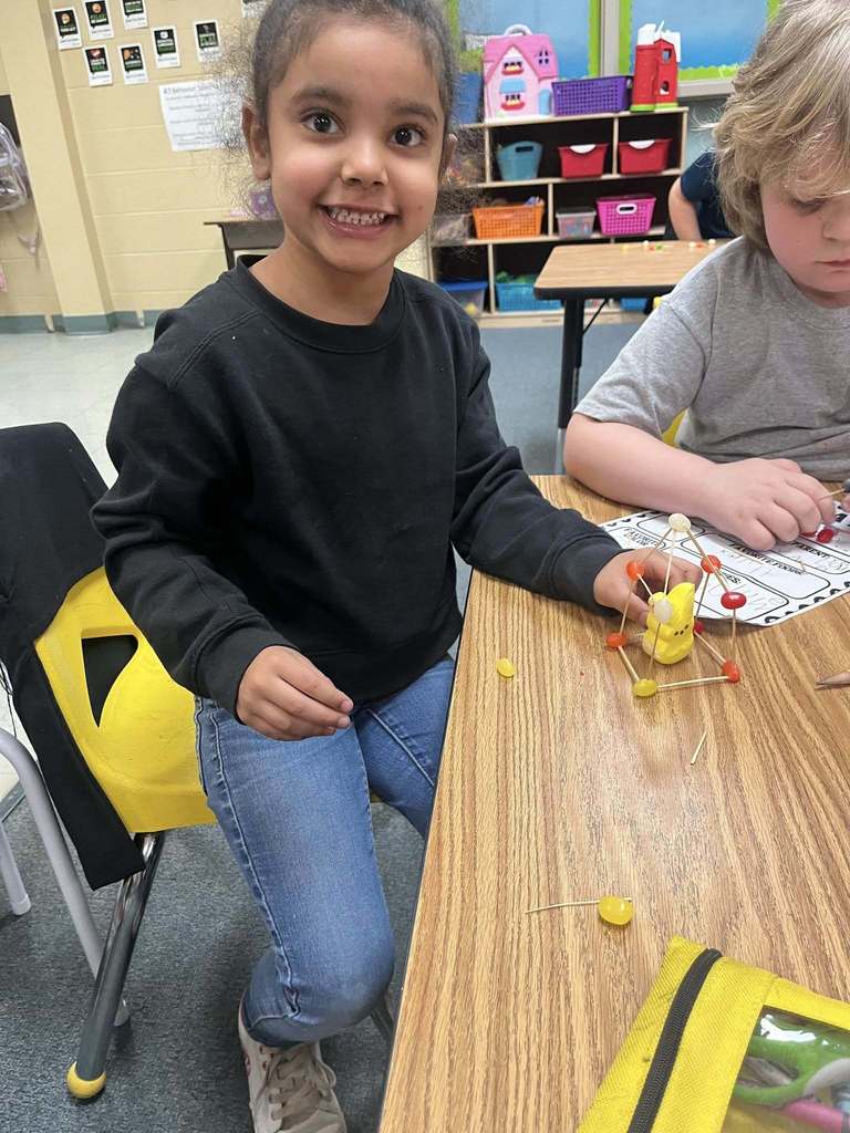 A student holding an easter peep inside a house she made of toothpicks and jelly beans.