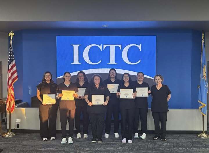 A group of nine individuals in black uniforms, holding certificates, pose on a stage in front of an ICTC backdrop.
