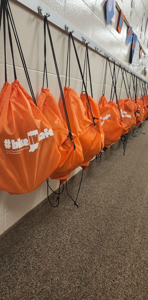 Orange Backpacks hanging on hooks on a wall.