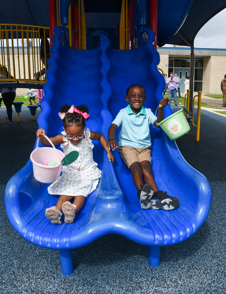 a boy and a girl sliding down side-by-side with baskets of easter eggs