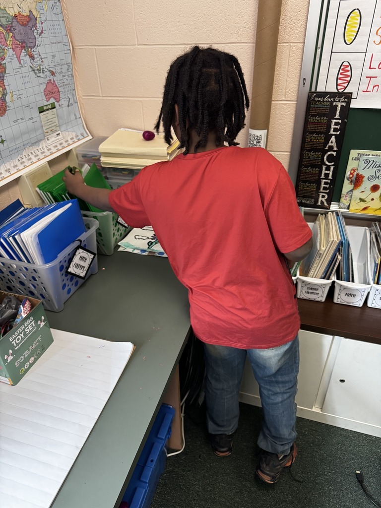 A student in  red shirt hiding an egg in between folders in the classroom. 