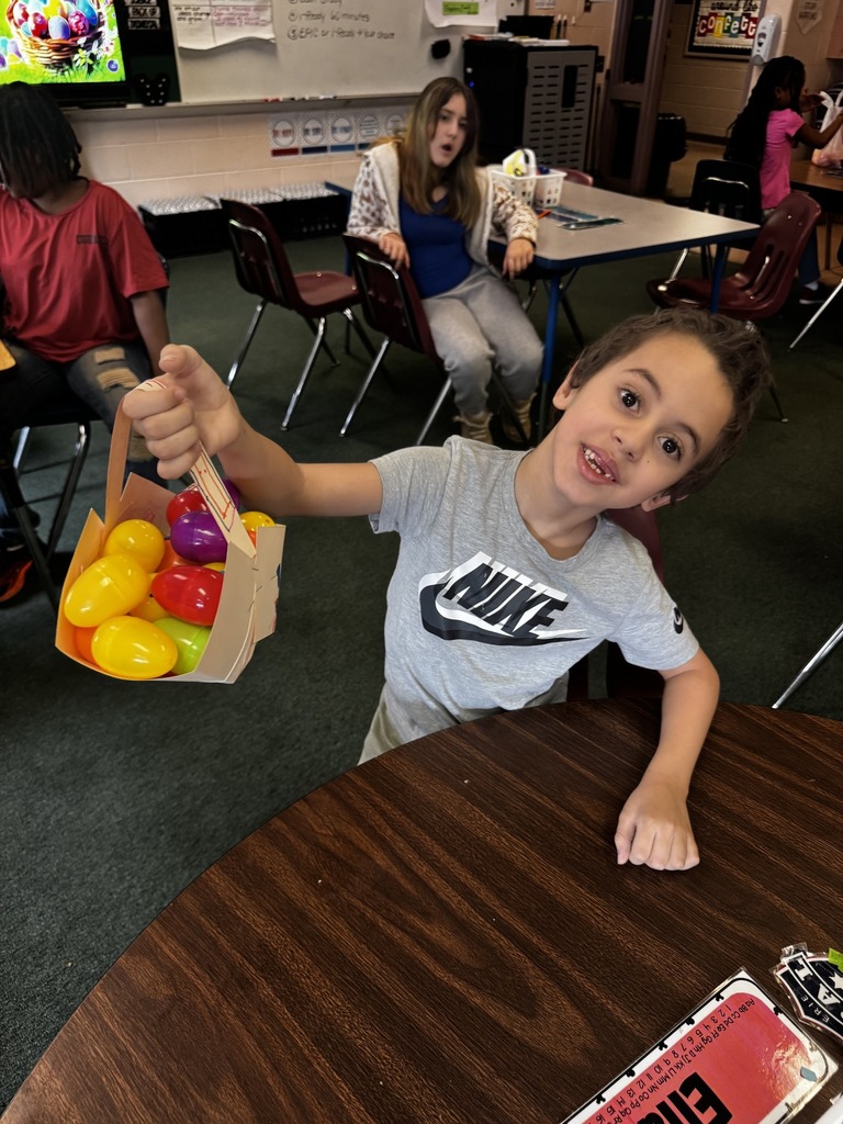 A young kid in a gray Nike shirt is holding a paper basket with colorful eggs in it. 