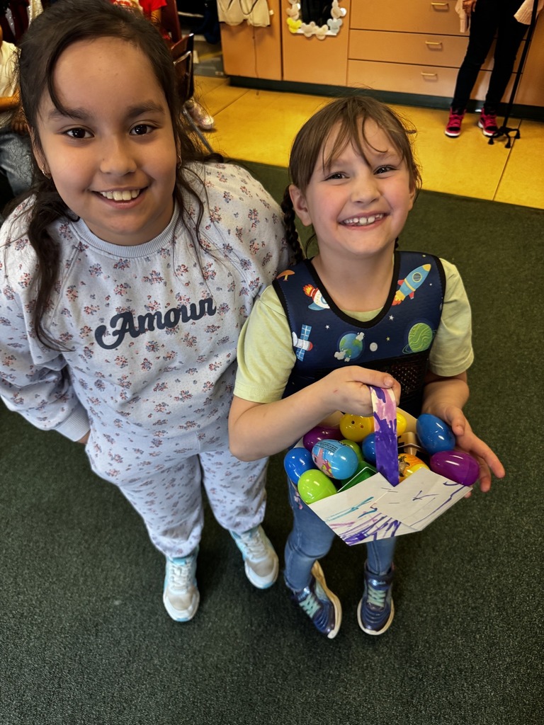 Two students pose for a photo while one is holding a paper basket with colorful eggs in it. 