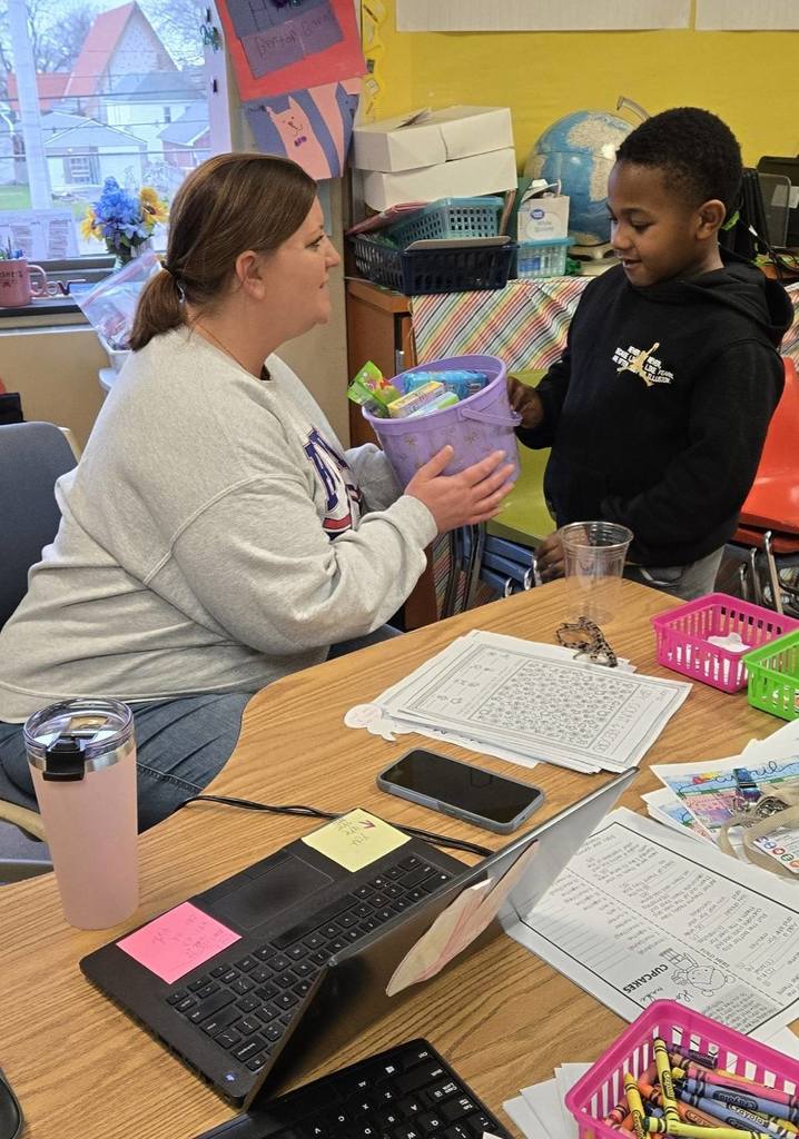 A teacher giving her student a purple easter basket. 