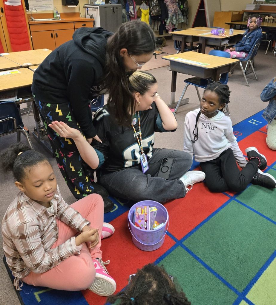 A student hugging a teacher while they all sit on the floor. 