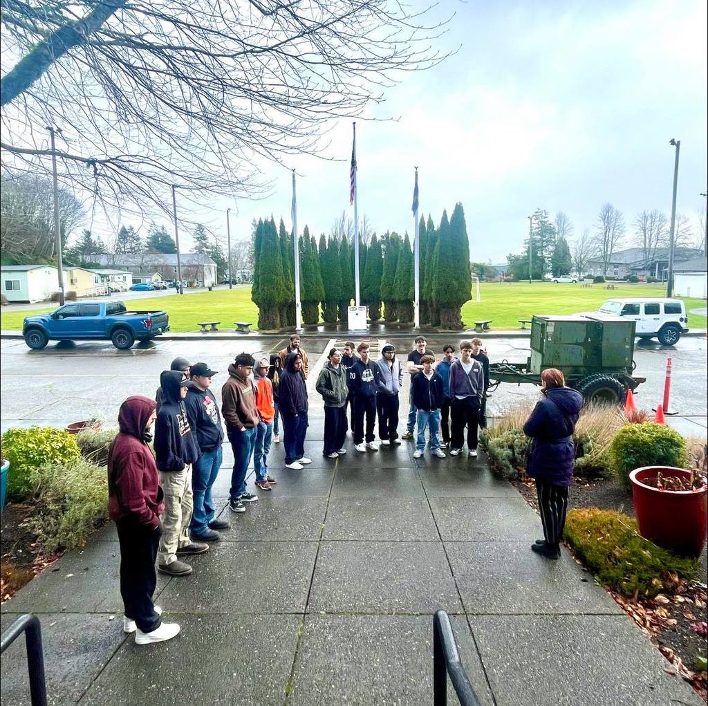 Students and teachers standing outside, listening to someone speak.