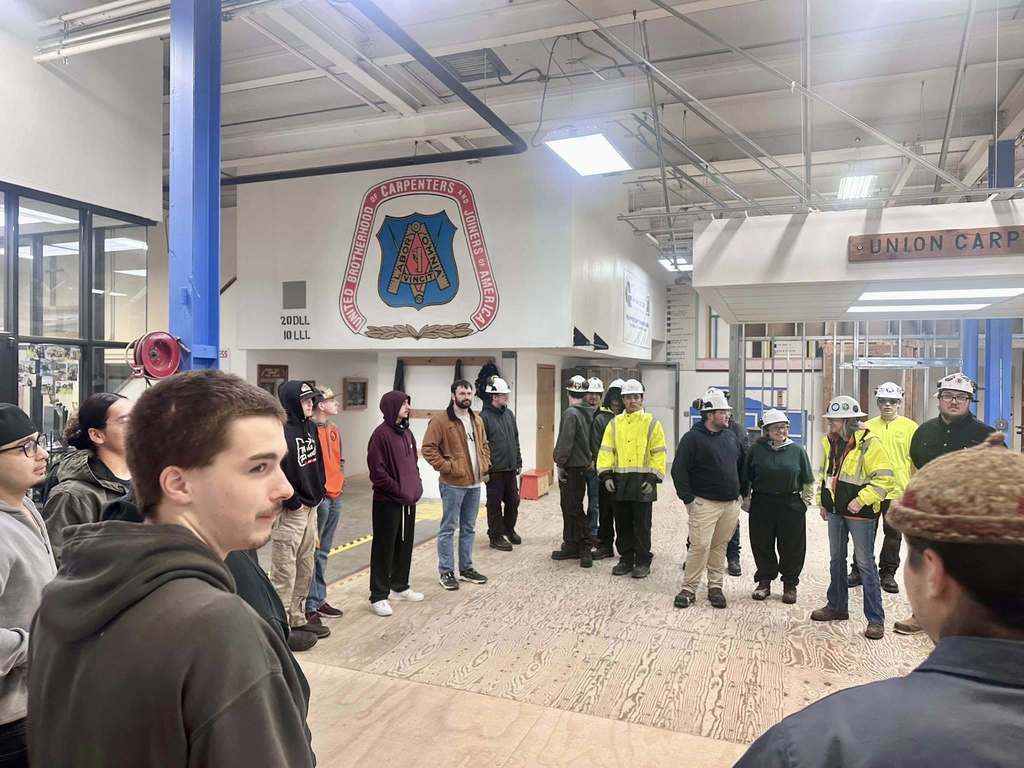 Students and teachers inside listening to people dressed in construction attire.