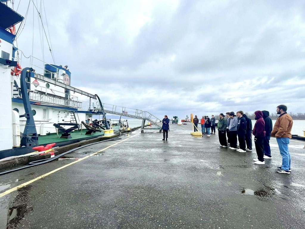 Students and teachers standing near and looking at a boat.