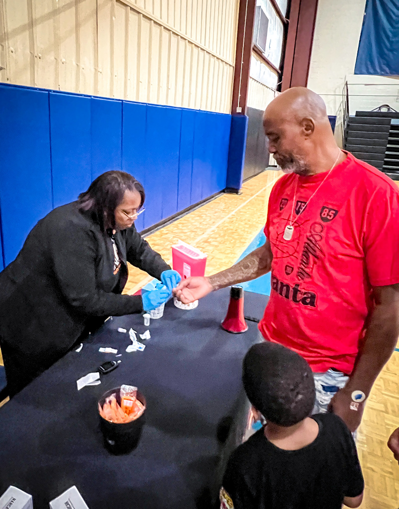 A man in a red shirt talks with a woman in black. Both are at a table with a boy.