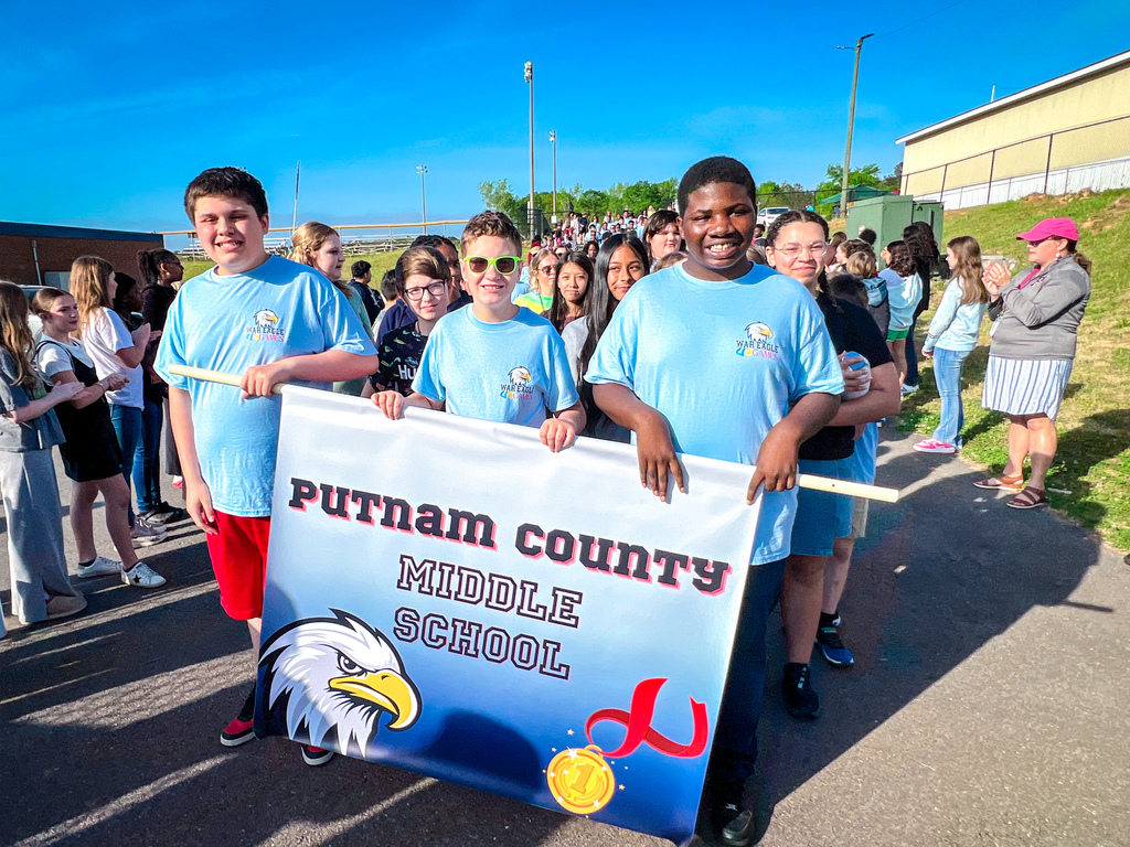 Several people in blue shirts walk in a parade, holding a banner with an eagle and text.
