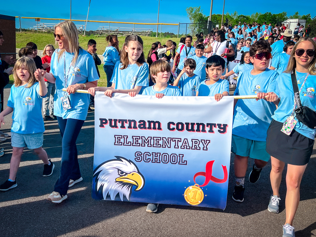 Group of students, teachers, and parents walking with a banner that reads "Putnam County Elementary School."