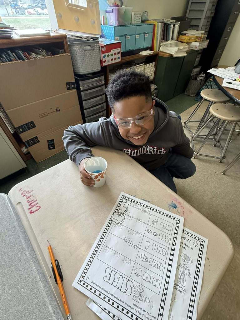 A young boy smiling while holding a cup of blue juice in one hand. 