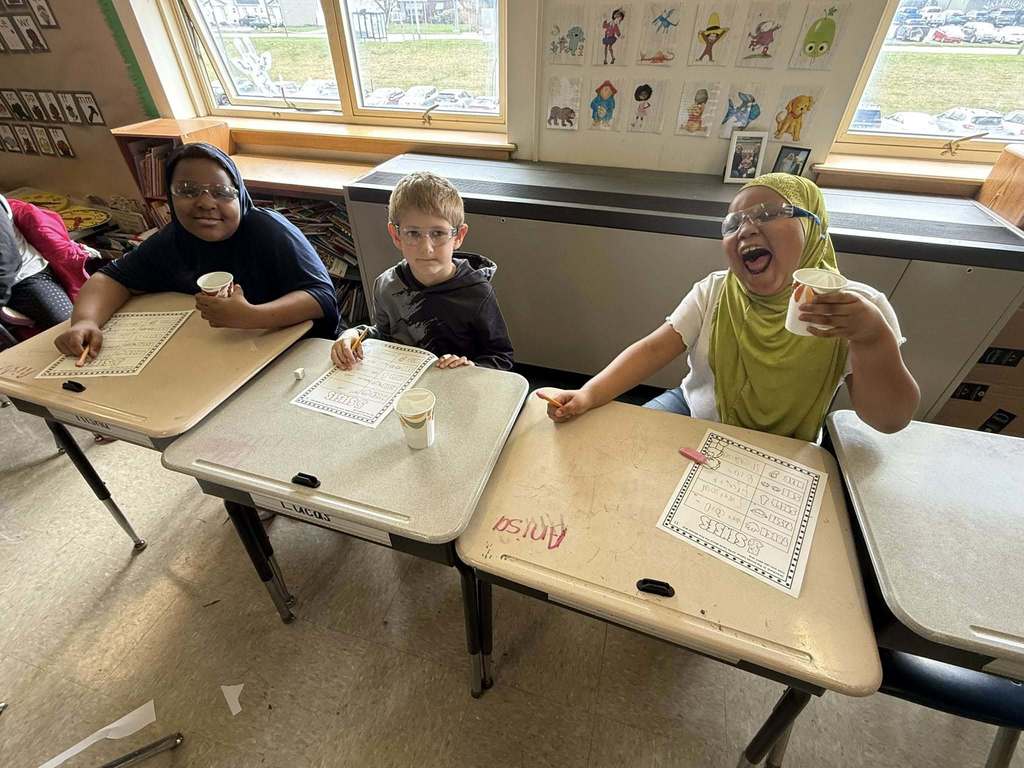 Kids posing in class while drinking from cups. 