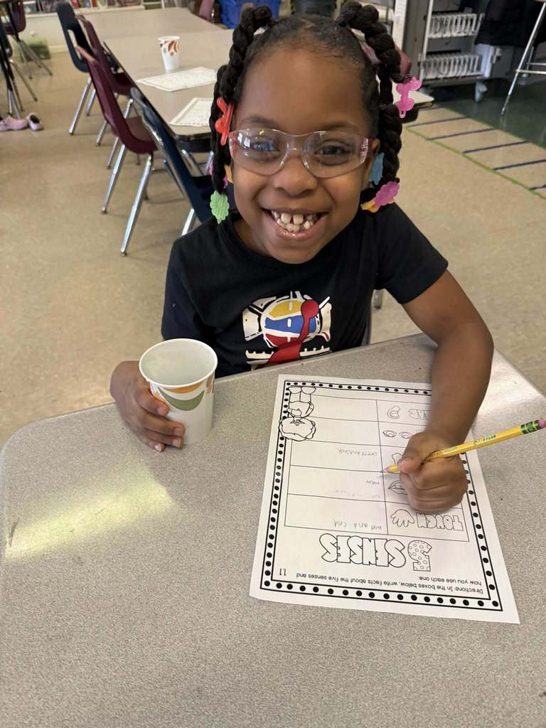 A young girl holding a cup in one hand and filling out her 5 senses worksheet with the other. 