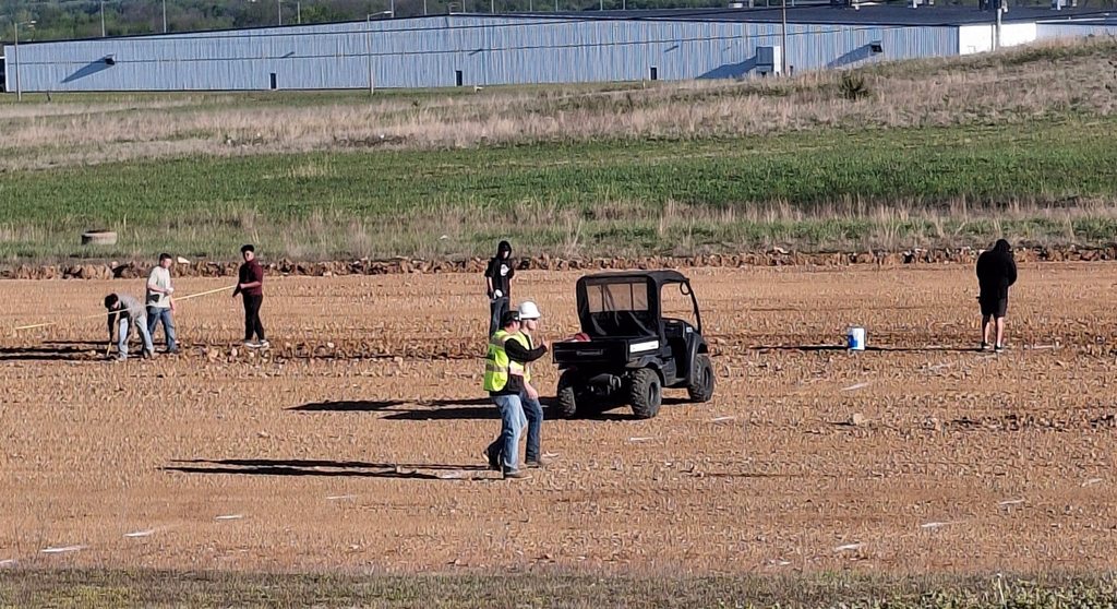 A group of people in a field with a golf cart and a building in the distance.
