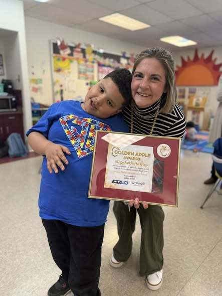 A teacher holding her Golden Apple Award and standing next to her student. 