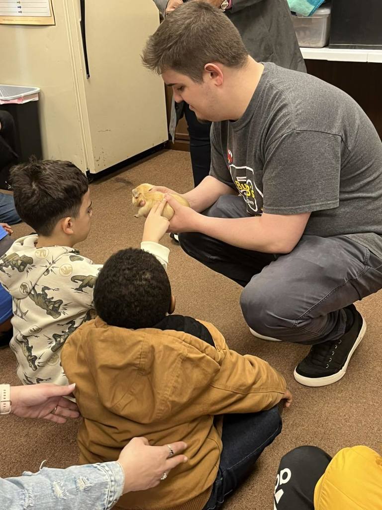 A man holding an hamster as students pet it. 